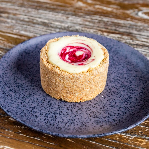 A round dessert with a crumbly crust, white cream, and a swirl of red berry sauce on a blue plate.