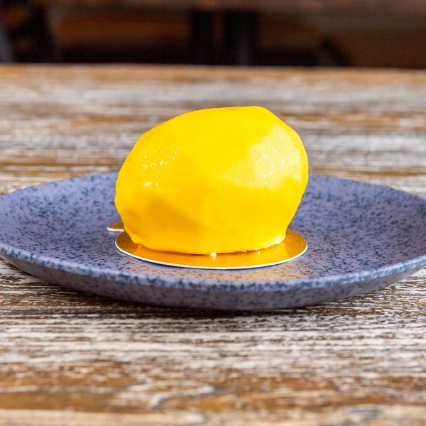 A bright yellow lemon-shaped dessert with a glossy glaze sits on a dark blue plate.