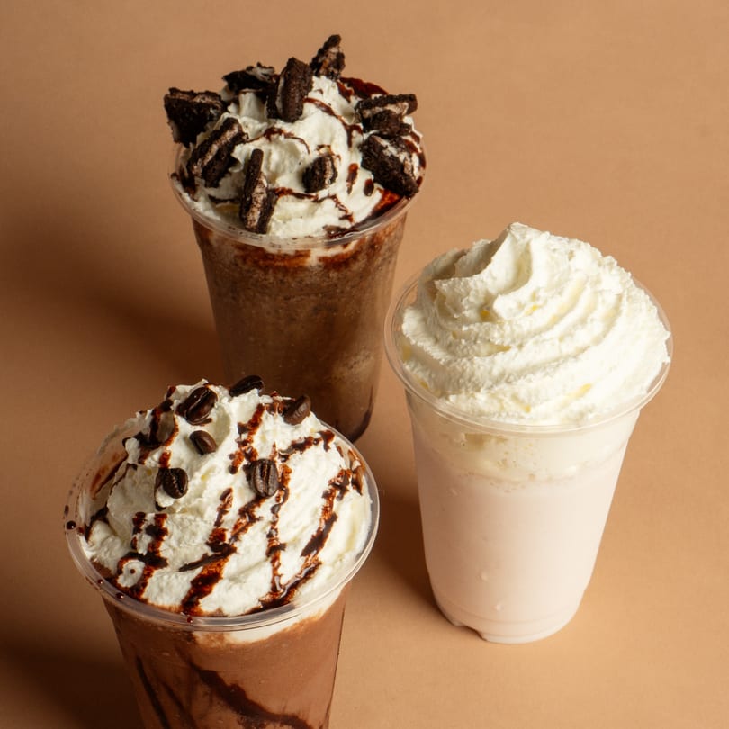 Three Rendezvous International Cafe milkshakes: two chocolate with whipped cream and toppings, one vanilla with whipped cream.