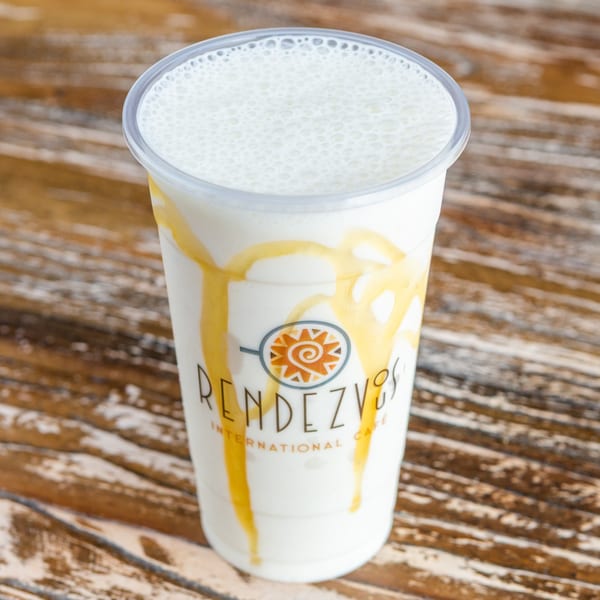 A Rendezvous International Cafe milkshake with caramel drizzle on a wooden table.