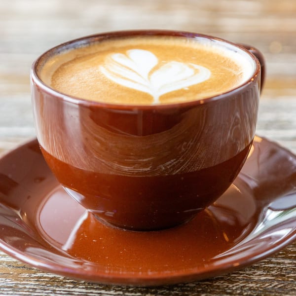 A brown ceramic cup of latte with heart-shaped foam art sits on a matching saucer.