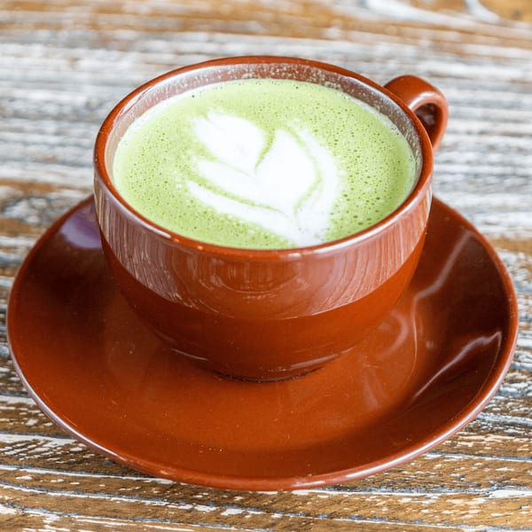 Matcha latte with latte art in a brown cup and saucer on a rustic wooden table.