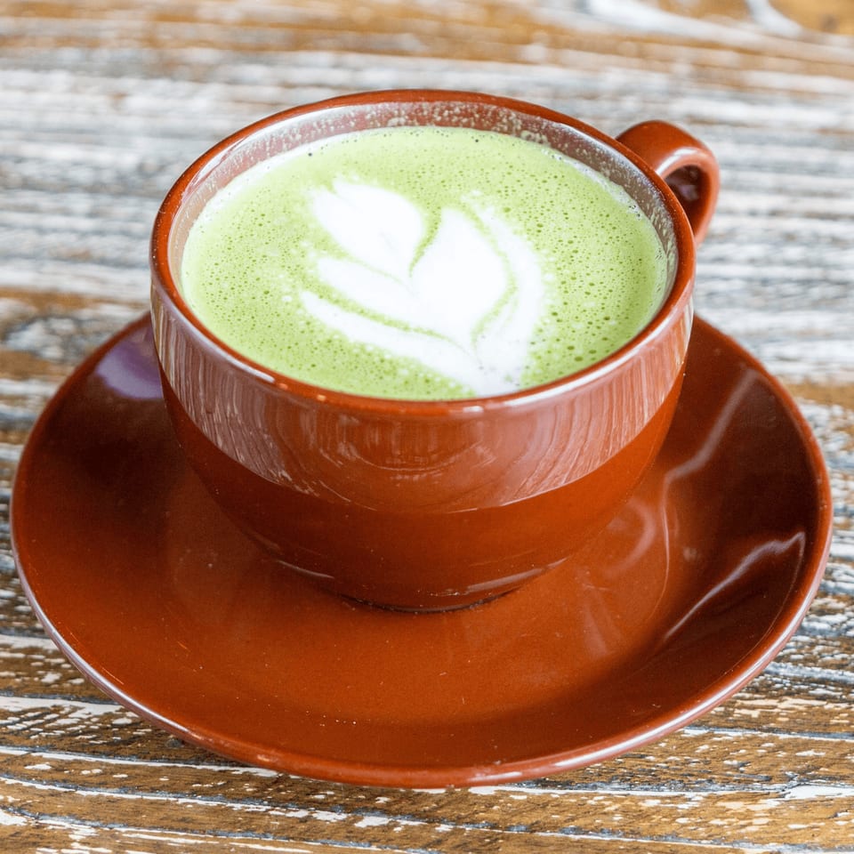 Matcha latte with latte art in a brown cup and saucer on a rustic wooden table.
