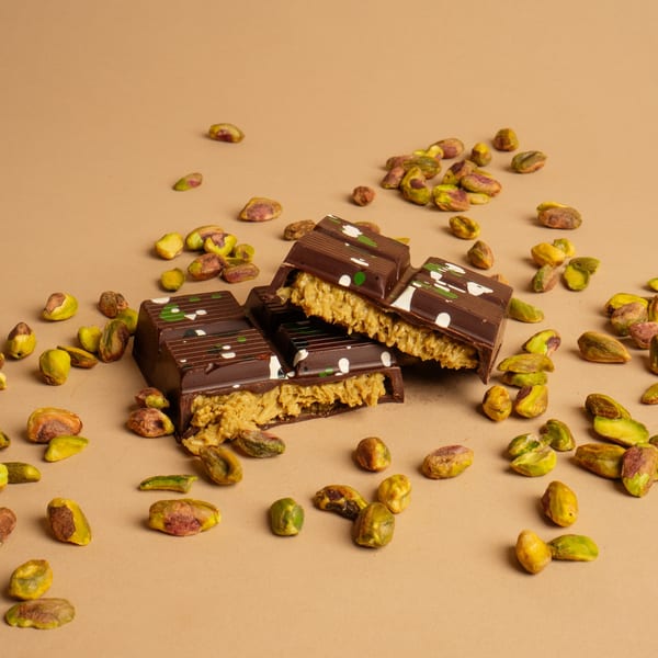 Broken chocolate bars with creamy pistachio filling and scattered pistachios on a tan surface.