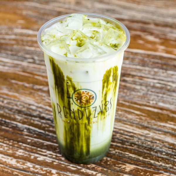 Iced matcha latte with Rendezvous International Cafe logo on a rustic wooden table.