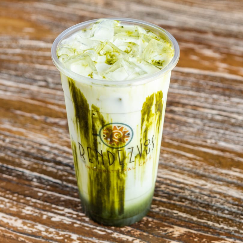 Iced matcha latte with Rendezvous International Cafe logo on a rustic wooden table.