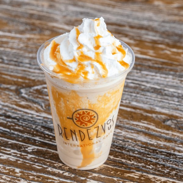 Rendezvous International Cafe's caramel frappe with whipped cream and caramel drizzle on a wooden table.