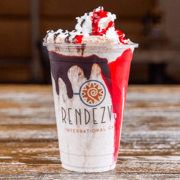 Rendezvous International Cafe's milkshake with whipped cream, chocolate, and strawberry syrup on a wooden table.