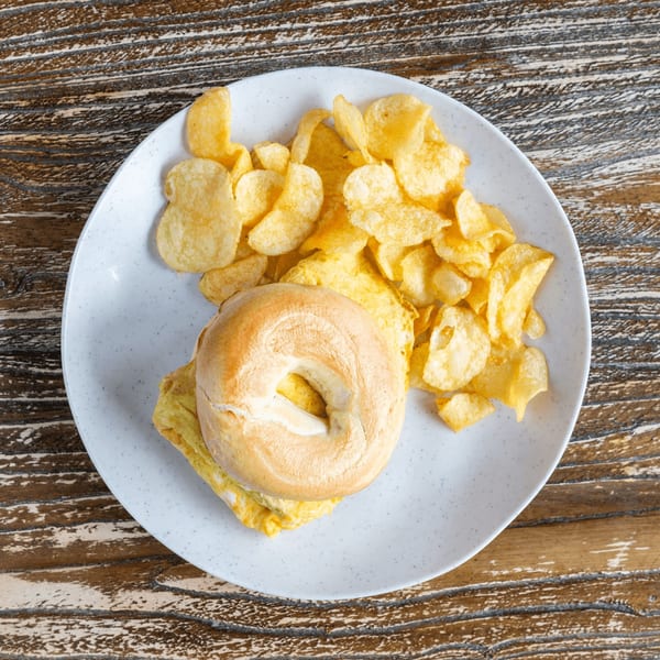Bagel with scrambled egg and a side of potato chips on a white plate.