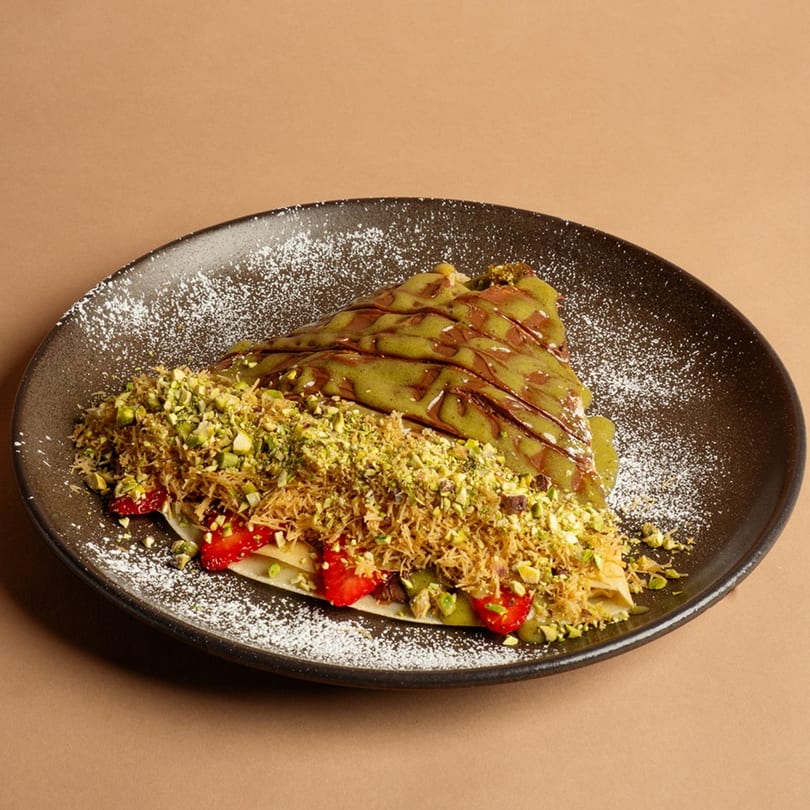 A Rendezvous International Cafe crepe with pistachio sauce, chocolate drizzle, strawberries, and crushed pistachios.