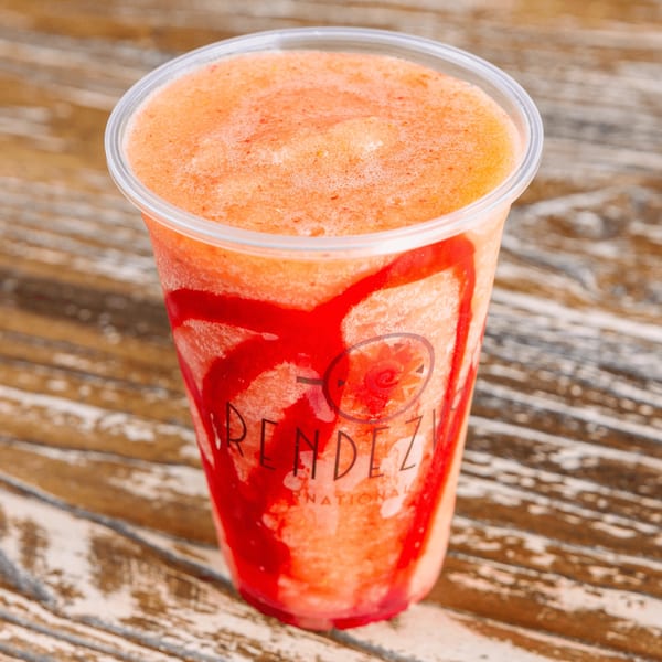 A Rendezvous International branded plastic cup filled with a vibrant orange and red swirled smoothie.