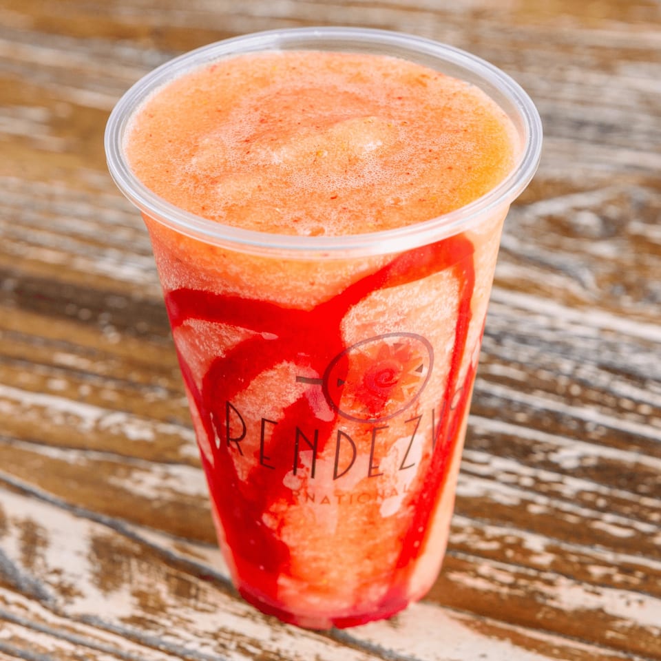 A Rendezvous International branded plastic cup filled with a vibrant orange and red swirled smoothie.