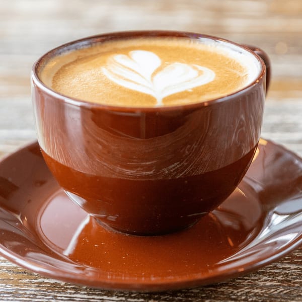 A brown mug of latte with heart-shaped latte art sits on a matching saucer.