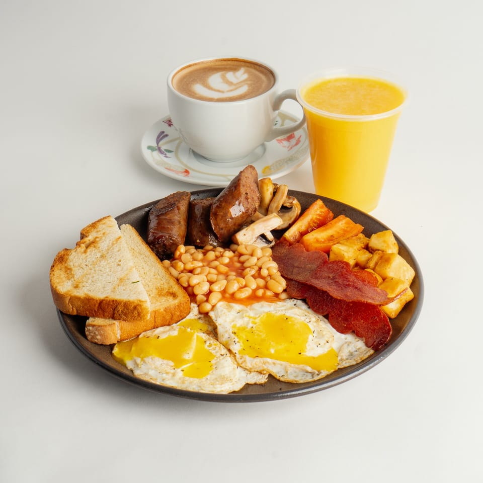 A full English breakfast with eggs, bacon, sausage, beans, toast, and coffee with latte art.