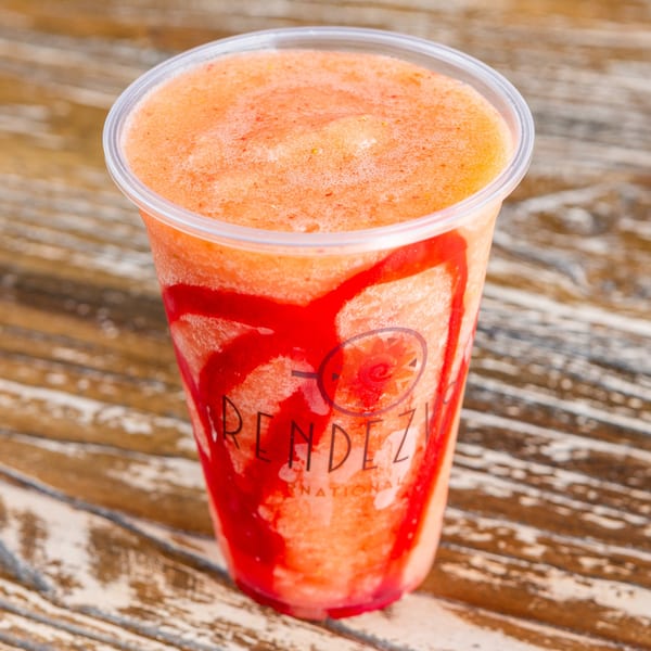 A Rendezvous International branded plastic cup filled with a peach-colored smoothie and red syrup.