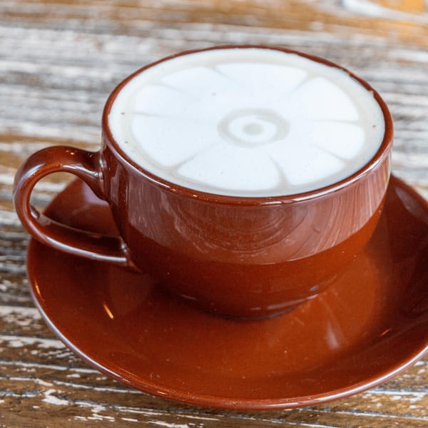 A brown cup and saucer with a latte featuring intricate foam art on a wooden table.