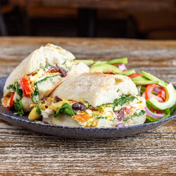 Two halves of a breakfast sandwich with eggs, spinach, and peppers, served with a side salad.