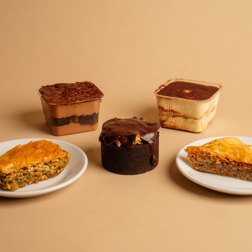 Assortment of Rendezvous International Cafe desserts: two baklava slices, a chocolate cake, and two layered parfaits.